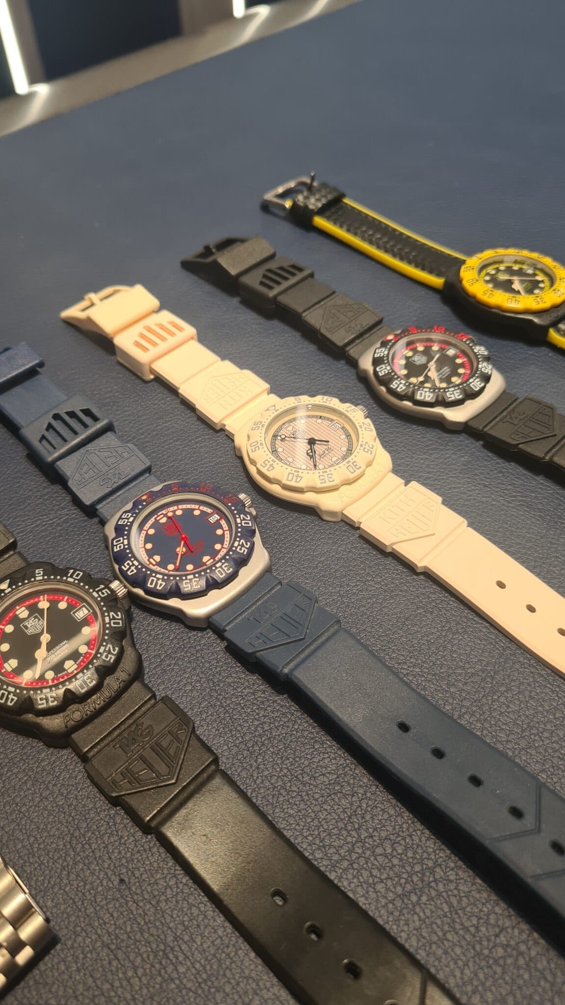 a line of TAG Heuer F1 watches from the first series with blue plastic cases and straps as well as black adn red, all on a blue table