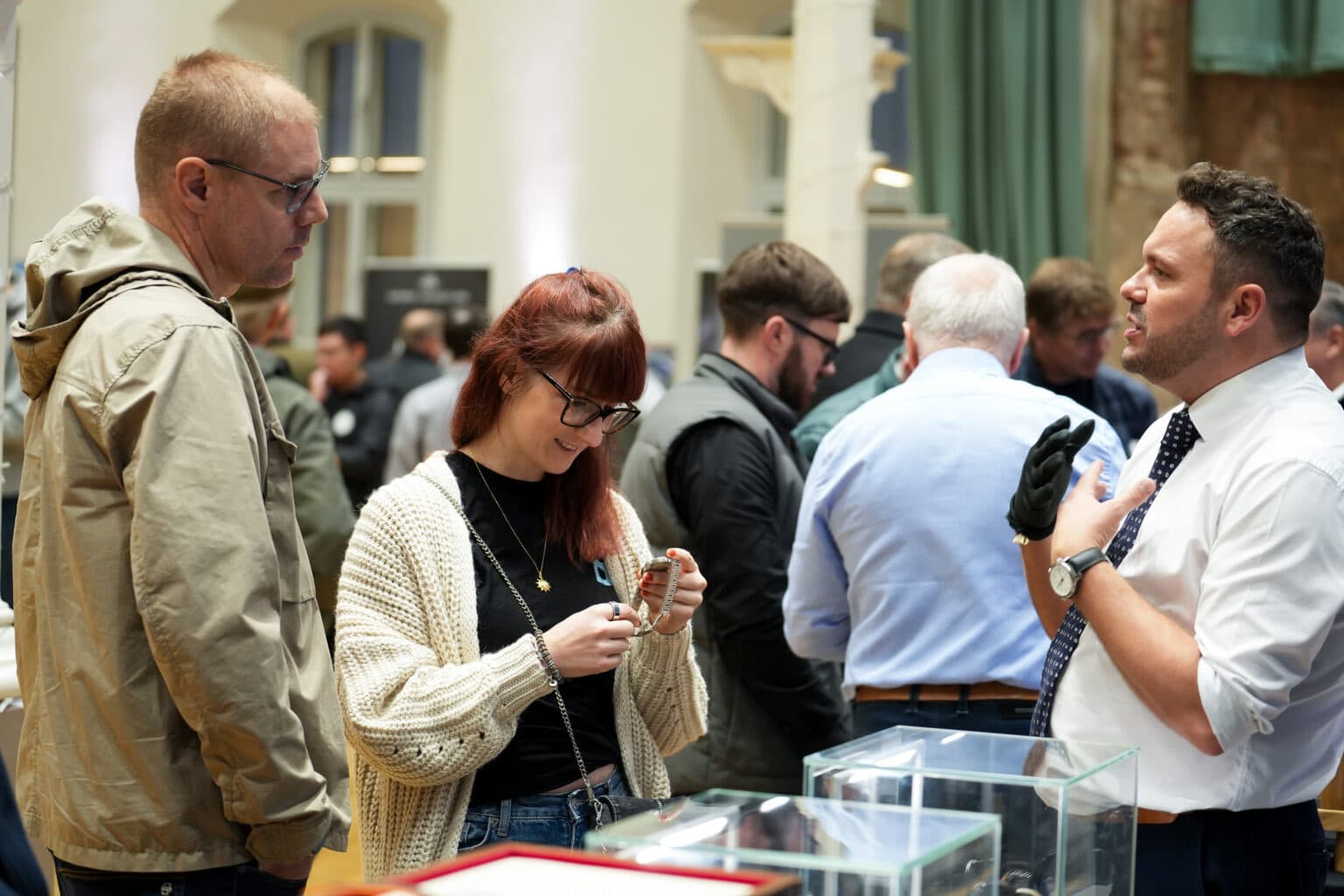 a young couple examining a watch at The Manchester Watch Show, leaning over a table full of watches with a man in white shirt explaining how it works