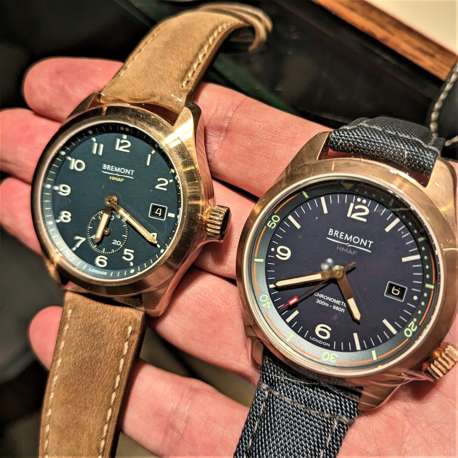 Two bronze cased watches from Bremont with green adn blue dials, clear numerals and date windows on a brown and blue strap.