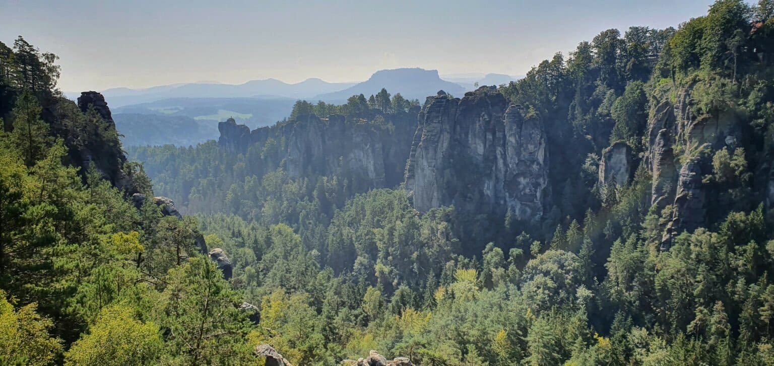 a wide raning forest view over gre cliffs and hills with a hazy sky above it