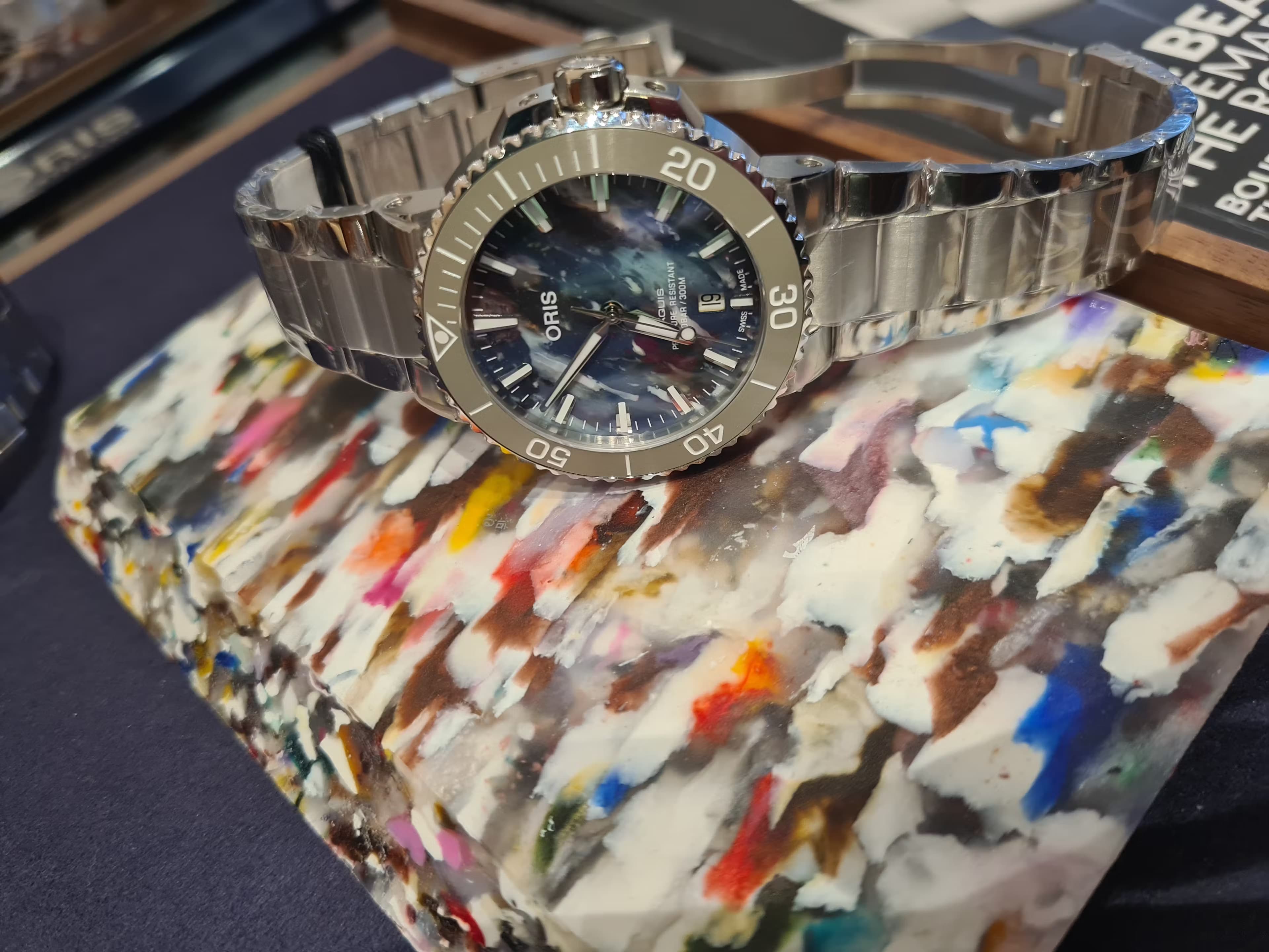 The Oris Aquis Upcycle sitting on top of a block of the recycled plastic used to make the dial of this watch.