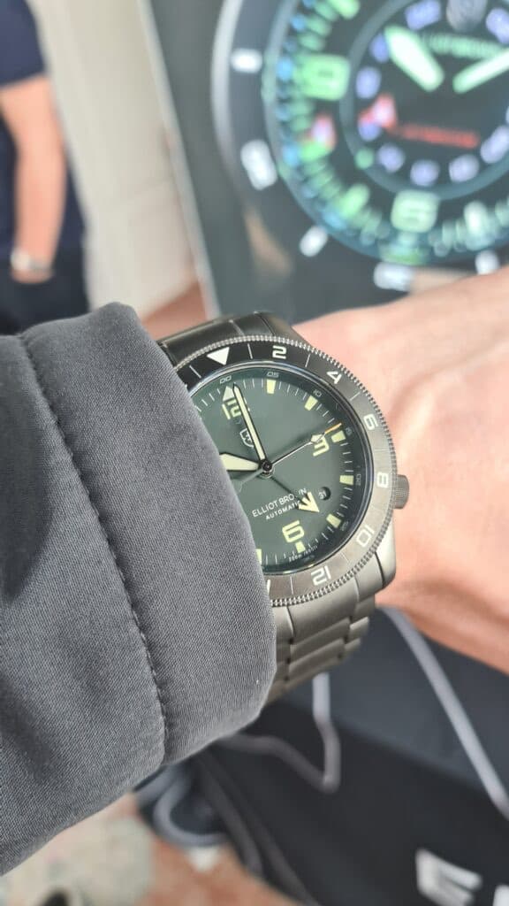 elliot brown tool watch with a green dial and grey bezel on a wrist with a grey coat cuff