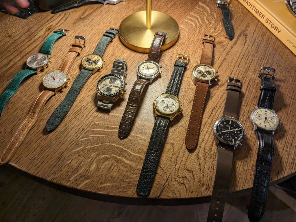 A group of vintage Chronographs on a brown table with different cases in gold and steel, and different straps.