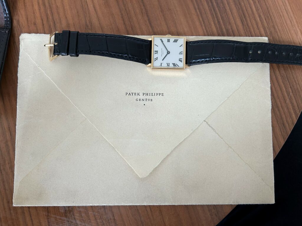 a watch at the top of an envelope on a table, with the envelope featuring the barnd name patek philippe