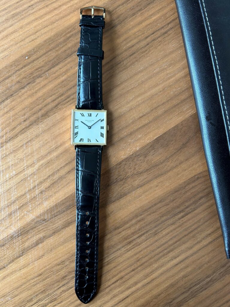 square gold patek philippe watch on black leather strap on a wooden table