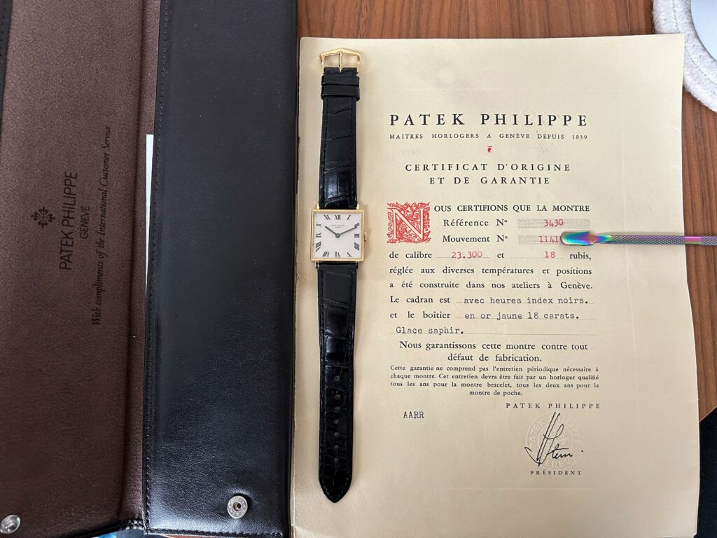 a watch, a watch pouch in black leather, and a certificate of authenticity form patek philippe with the numbers obscured