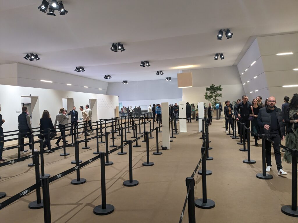 large hall with queieing system for zirport style security with beige walls and carpets and people in the queue