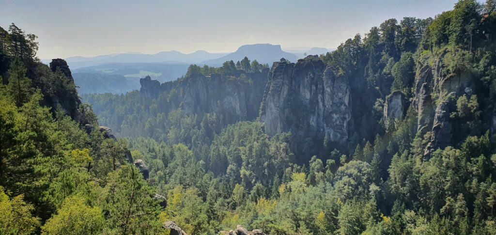 a wide raning forest view over gre cliffs and hills with a hazy sky above it