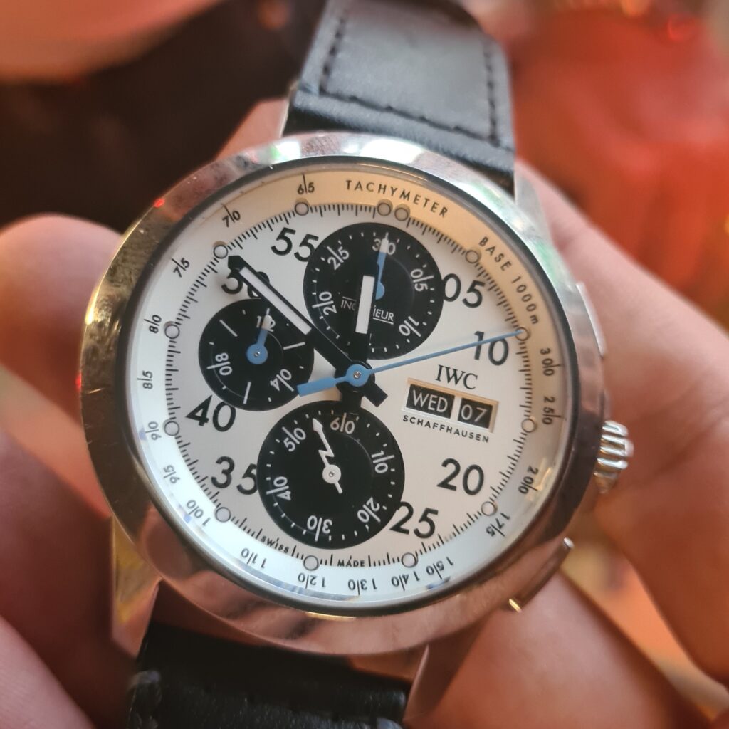 a roudn steel IWC lewis hamilton watch with white dial, large black subidals, unusualy hands, and ay date feature at 3 o'clock