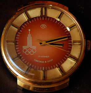 a red and gold watch wtih blakc hands and hour markers made for the moscow 1980s olympics with the logo and rings on the left hand side of the dial made by Slava